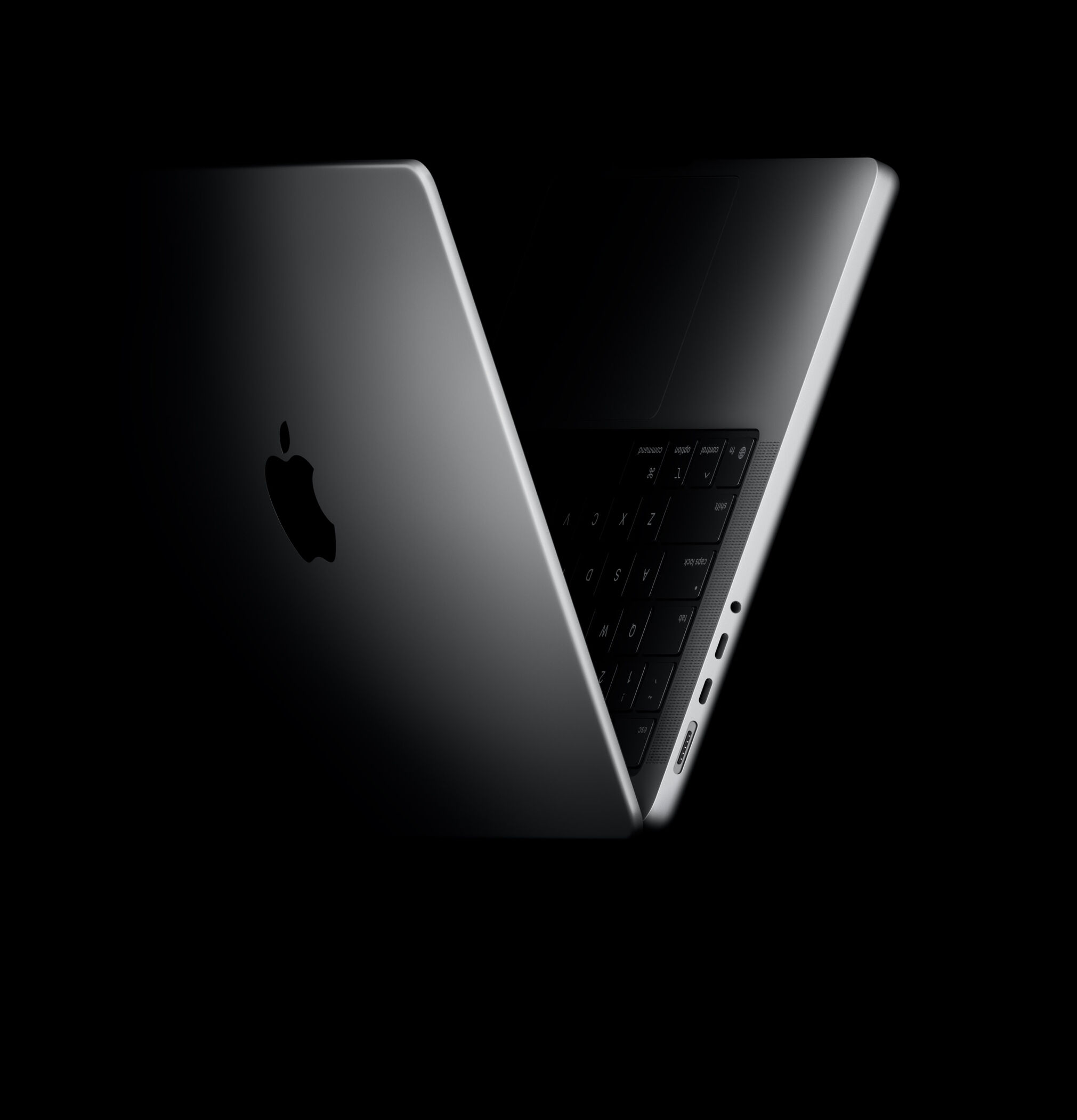 MacBook Pro half-open, its aluminum lid and keyboard edge glowing against a black room
